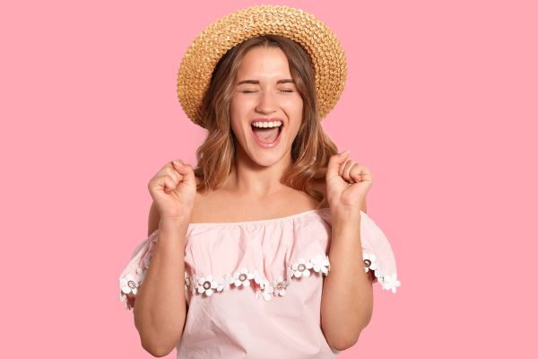 como lidar com a insegurança mulher com chapéu sorrindo com vestido rosa e fundo rosa