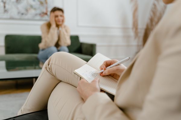 terapia dus mulheres sentadas e uma com caneta e caderno e outra com mão no rosto
