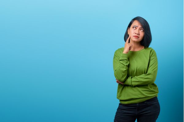 mercado de trabalho mulher olhando pra cima com o dedo no rosto pensando e no fundo parede azul