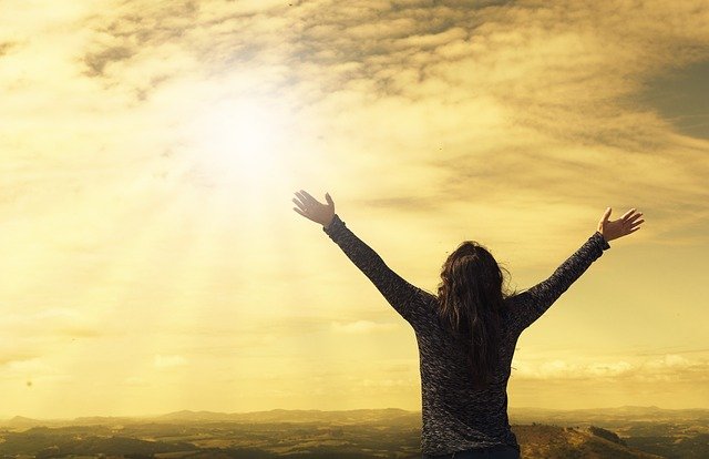 uma mulher com braços abertos olhando para o sol