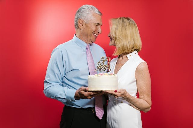 Uma senhora acma de 50 anos segurando um bolo junto com um homem acima de 50 anos