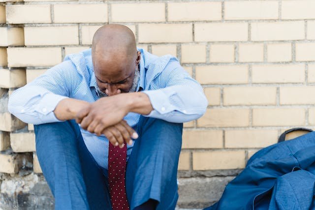 uma homem careca sentado olhando para o chão e chateado