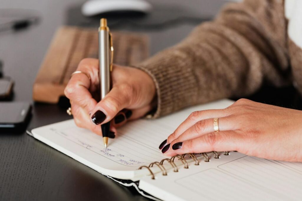 Uma mão de uma mulher com uma caneta escrevendo no caderno