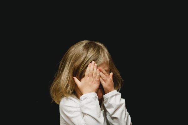 criança com as duas mãos nos olhos chorando