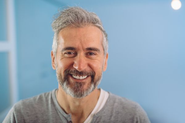 homem de cabelo grisalho sorrindo com camisa cinza