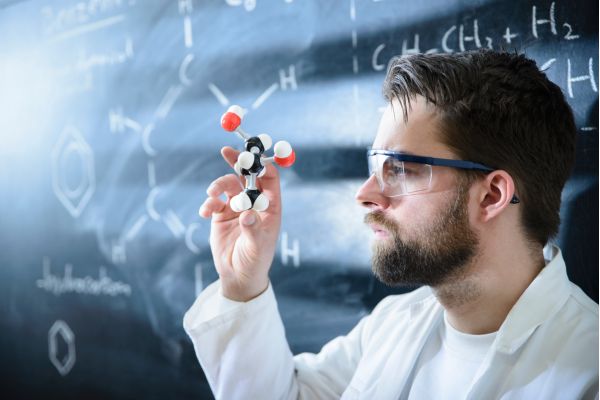 cientista de óculos com qudaro cheio de fórmulas e em sua mão umas bolinhas