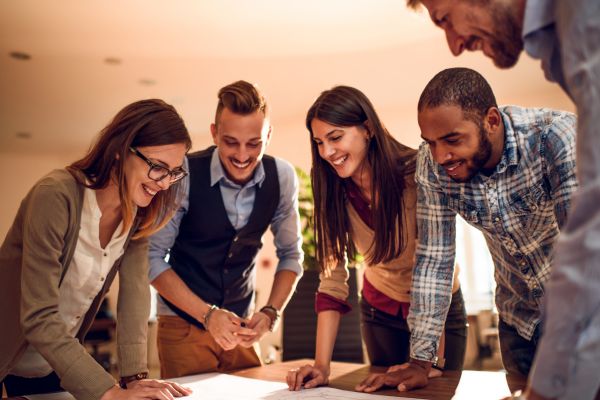 textos motivacionais trabalho em equipe 3 homens e 2 mulheres olhando pra mesa e sorrindo