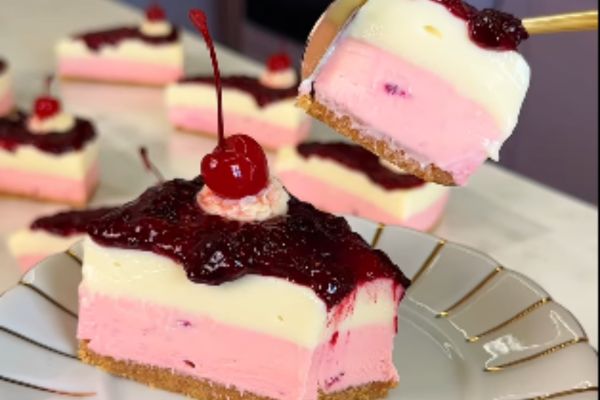 dois pedaços de torta de mousse de morango e limão com cobertura de geleia de frutas vermelhas e cereja.