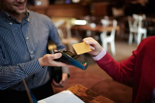 Cartão Black: O Passaporte pra uma Vida de Luxo e Exclusividade duas pessoas. um com maquina de cartão e outra passando o cartão de credito amarelo